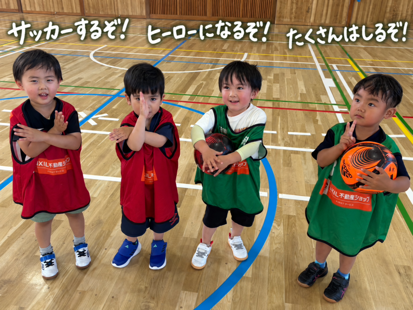 体育館でボールを持ちポーズを決める4人の子どもたち。サッカーするぞ！ヒーローになるぞ！たくさんはしるぞ！